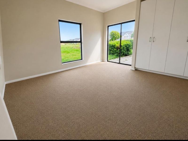 A bright, empty bedroom featuring neutral carpeting, built-in cupboards, and large windows with direct access to the garden area.