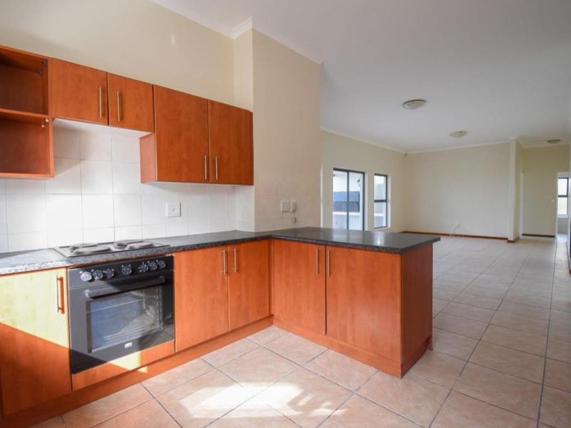 Open plan kitchen featuring wooden cabinetry, granite countertops, and built-in appliances, flowing into a spacious, tiled living area.