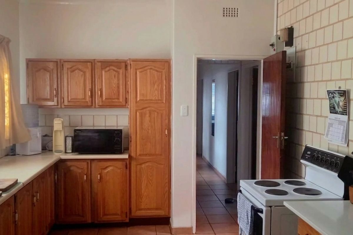A functional kitchen featuring traditional wooden cabinetry, tiled splashbacks, and a freestanding stove, offering a classic layout with direct access to the hallway.