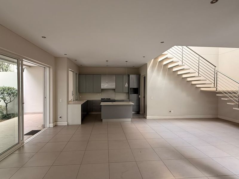Spacious open-plan living area featuring a modern kitchen with island, sleek cabinetry, and a contemporary staircase leading to the upper level.