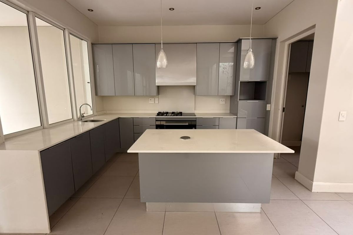 Modern kitchen featuring sleek grey cabinetry, stone countertops, a central island, and integrated appliances, offering a clean and functional culinary space.