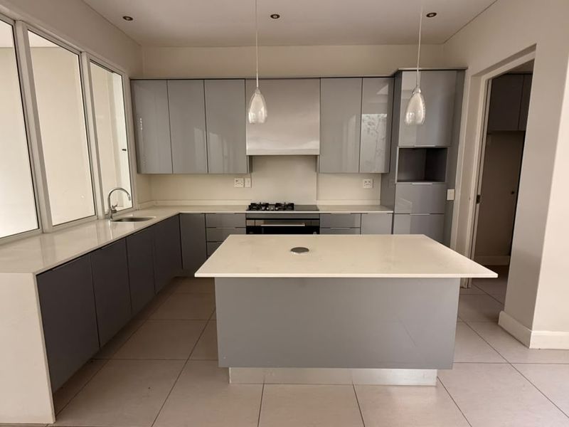 Modern kitchen featuring sleek grey cabinetry, stone countertops, a central island, and integrated appliances, offering a clean and functional culinary space.