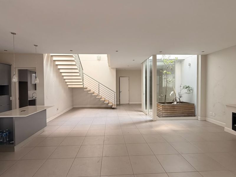 Spacious open-plan living area featuring a modern kitchen, central staircase, built-in fireplace, and a unique internal courtyard with natural light.