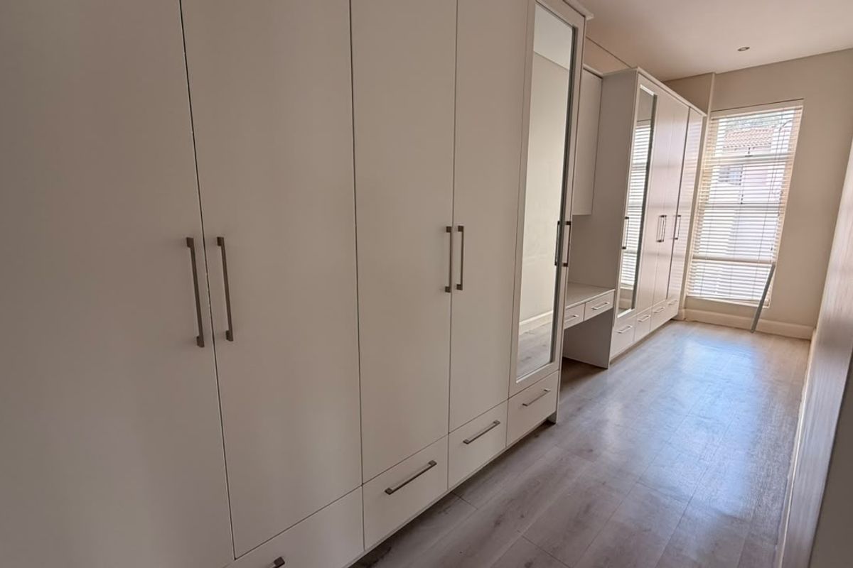 A bright bedroom featuring extensive built-in cabinetry with integrated vanity, mirrored doors, and modern laminate flooring.