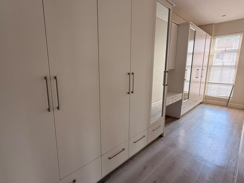 A bright bedroom featuring extensive built-in cabinetry with integrated vanity, mirrored doors, and modern laminate flooring.