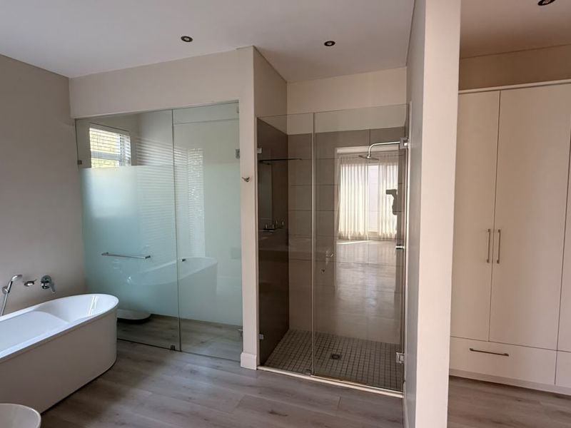 Modern bathroom featuring a sleek freestanding bathtub, a spacious glass-enclosed shower, and ample built-in storage cabinetry with contemporary finishes.