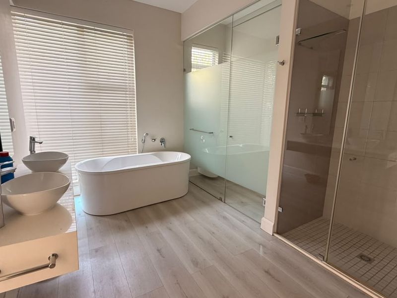 Modern bathroom featuring a freestanding bathtub, dual vessel sinks on a floating vanity, and a spacious glass-enclosed shower with tiled flooring.
