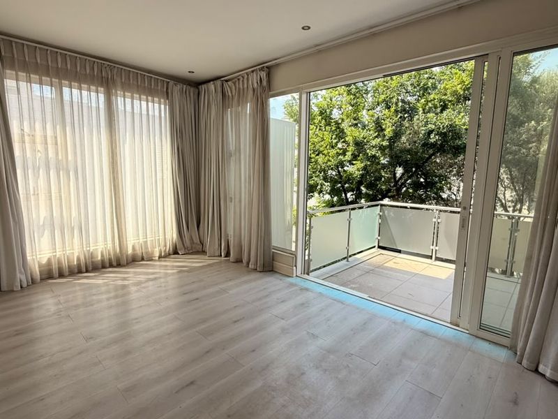 Bright and spacious living area featuring light laminate flooring, recessed lighting, and large sliding glass doors opening onto a private balcony.
