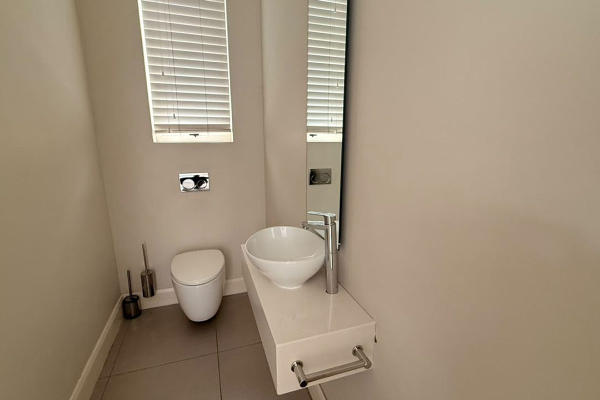 A modern, minimalist guest bathroom featuring a wall-mounted toilet, floating vanity with a vessel sink, and neutral tiled flooring.