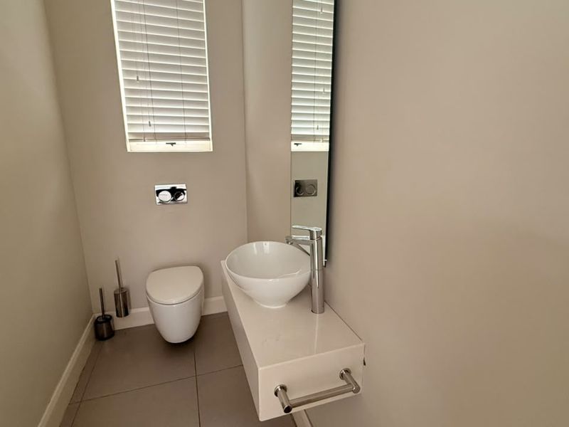 A modern, minimalist guest bathroom featuring a wall-mounted toilet, floating vanity with a vessel sink, and neutral tiled flooring.