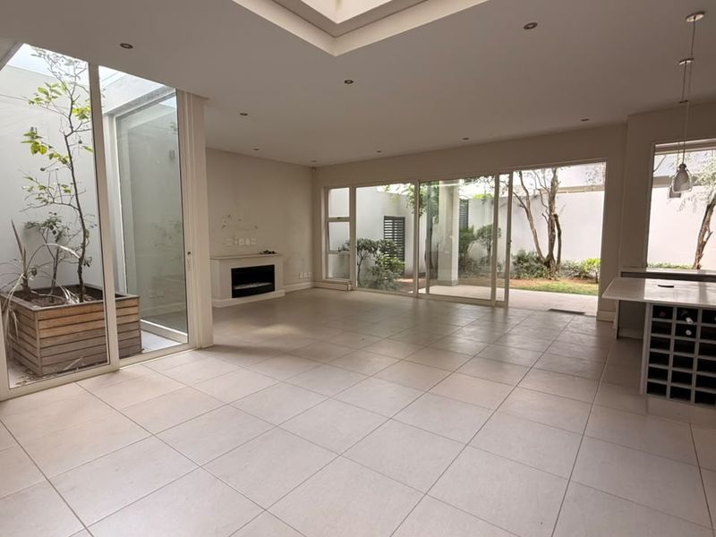 Spacious open-plan living area featuring tiled floors, a built-in fireplace, a central atrium, and large sliding doors opening to a private garden.