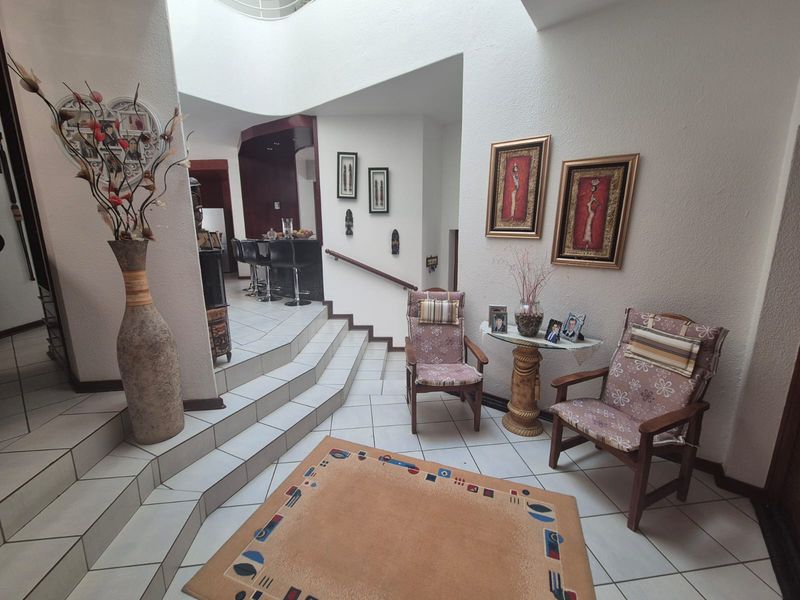 An inviting entrance hall featuring tiled flooring, a staircase with a handrail, and a view towards a built-in bar area.