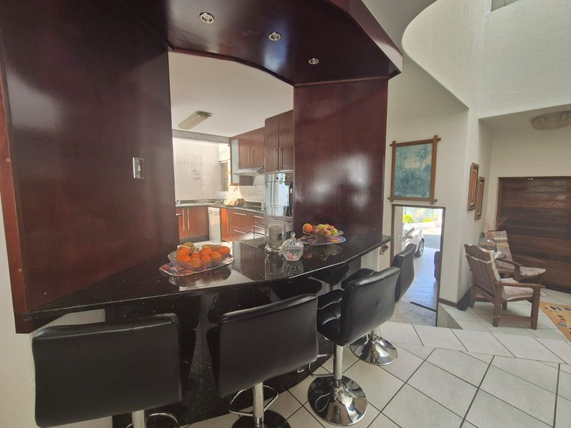 Open-plan living area featuring a dark wood breakfast bar with granite countertop, integrated kitchen cabinetry, and tiled flooring leading to a staircase.