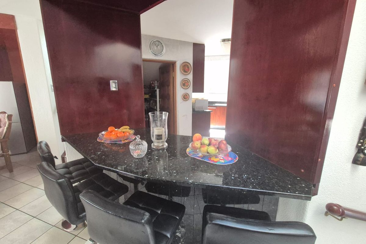 A kitchen area featuring a dark granite breakfast bar, built-in cabinetry, and tiled flooring, with an archway leading to a secondary prep space.