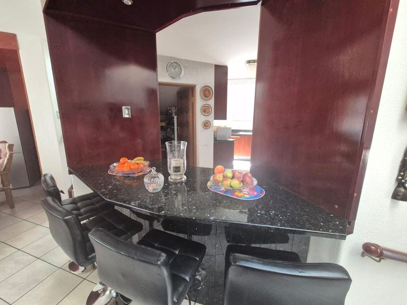 A kitchen area featuring a dark granite breakfast bar, built-in cabinetry, and tiled flooring, with an archway leading to a secondary prep space.