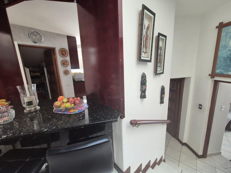 Open plan living area featuring a granite breakfast counter, tiled flooring, and a staircase with a wooden handrail leading to lower levels.
