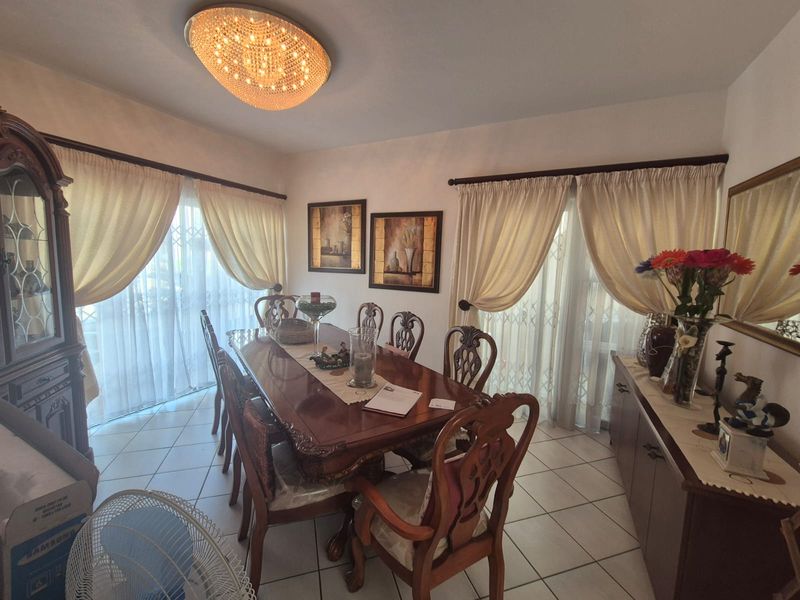 A formal dining room featuring ceramic floor tiles, a decorative crystal chandelier, and sliding glass doors with security gates providing access to the exterior.