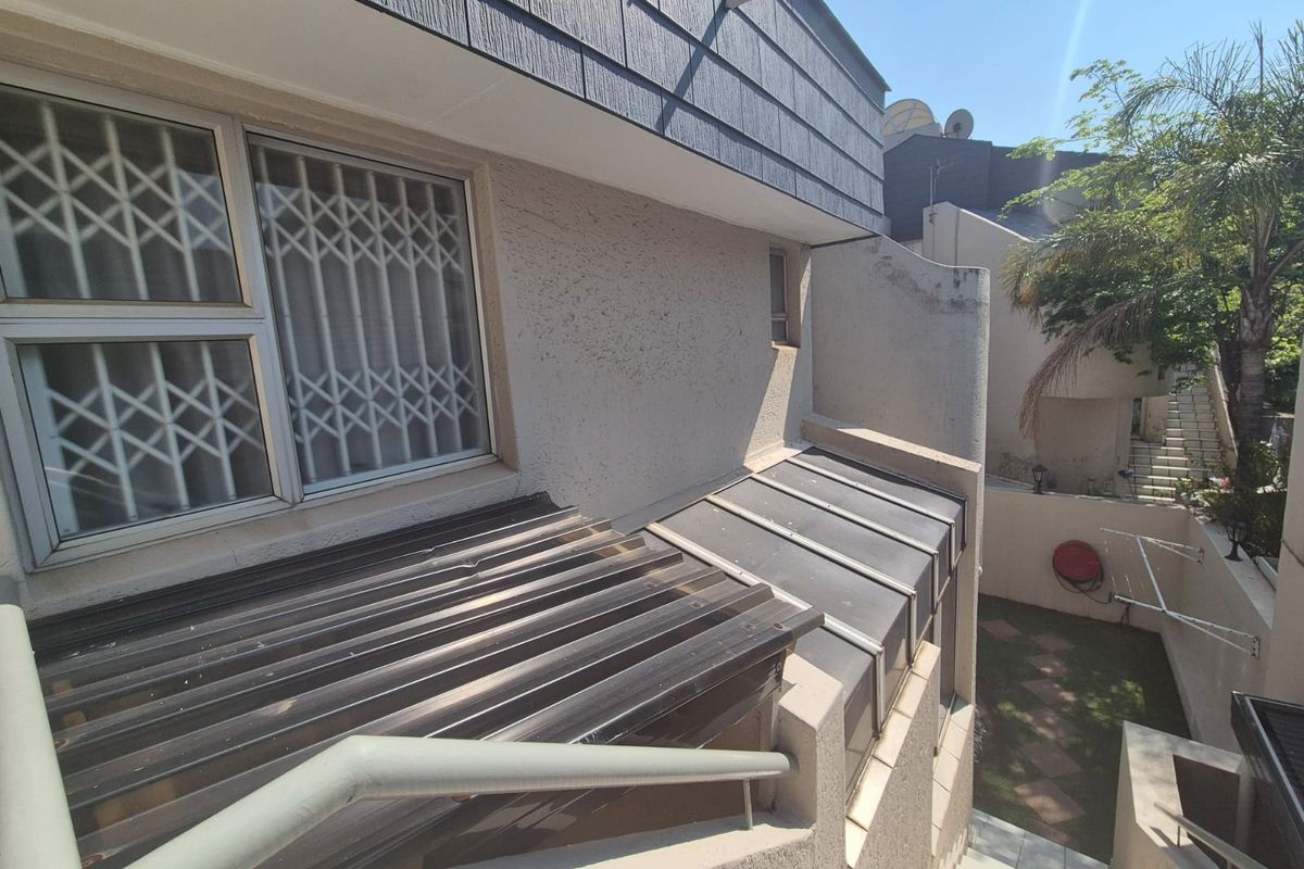 Rear exterior view of the property featuring a staircase, security gates on windows, and a small paved garden area.