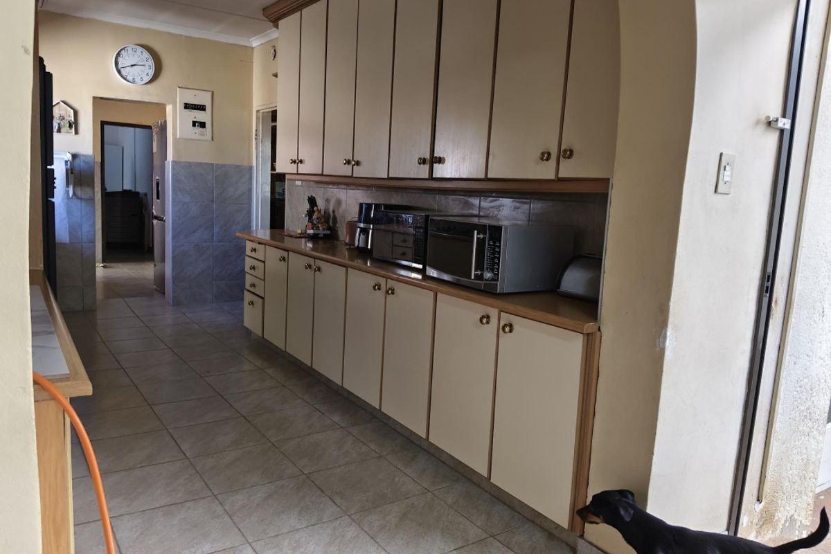 A functional kitchen featuring extensive built-in cabinetry, tiled flooring, and a tiled splashback, connected to adjacent living areas via an arched doorway.