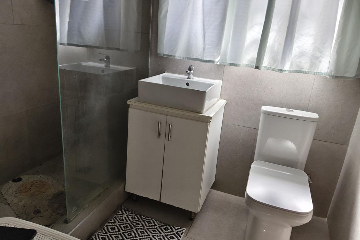 A modern bathroom featuring a vessel sink with vanity cabinet, a white toilet, and a glass-enclosed shower area with neutral wall tiling.
