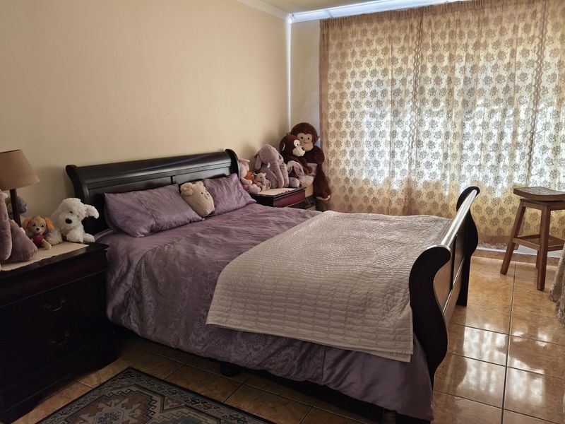 A bedroom featuring tiled flooring and large window with curtain treatments, providing a functional space for rest.