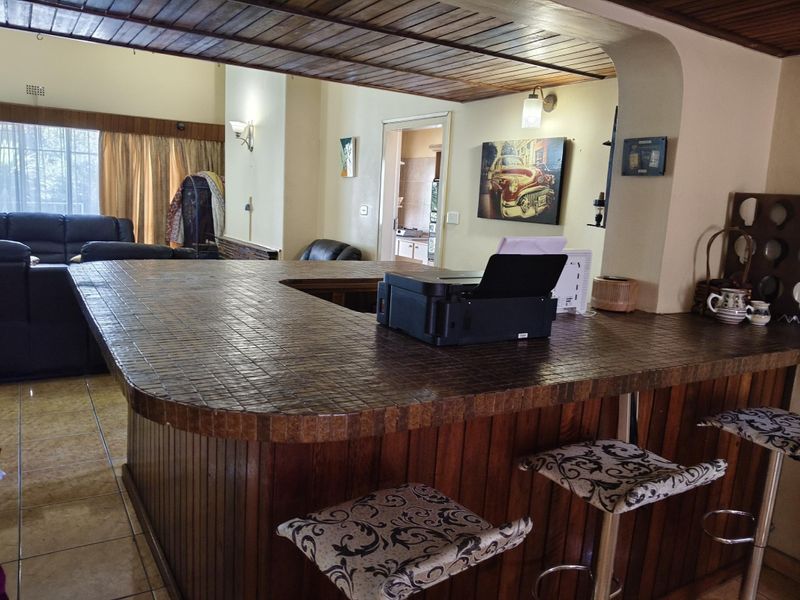 Open plan living area featuring a large tiled bar counter with timber paneling and a distinctive timber ceiling, connecting to adjacent living and kitchen spaces.