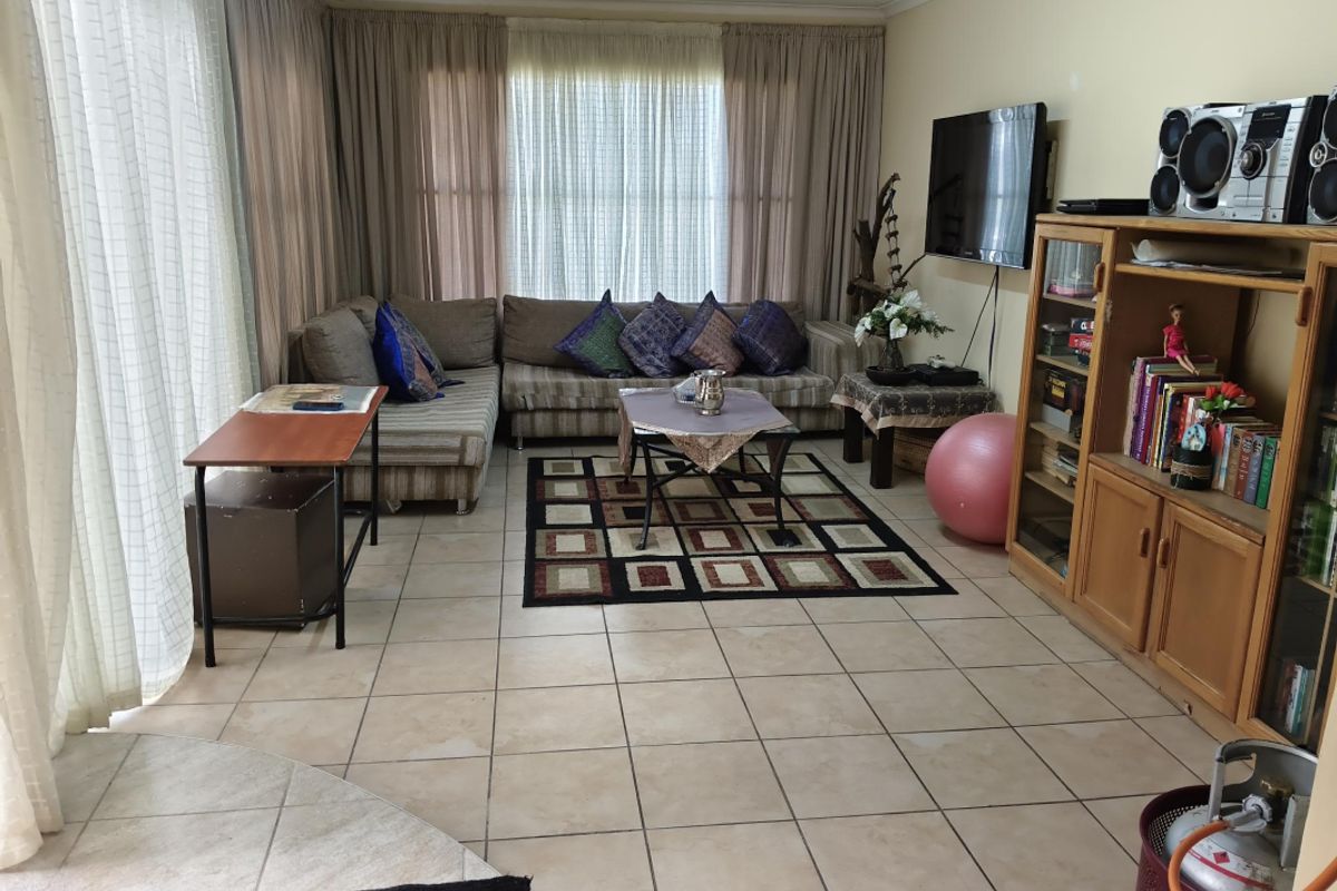 A spacious living room featuring neutral tiled flooring and large windows with full-length curtains, offering a functional and comfortable layout.