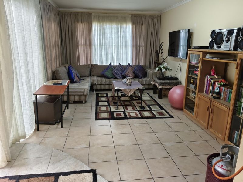 A spacious living room featuring neutral tiled flooring and large windows with full-length curtains, offering a functional and comfortable layout.