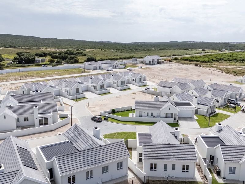 Aerial view of a modern residential estate featuring uniform white houses with grey tiled roofs, paved driveways, and landscaped surroundings.