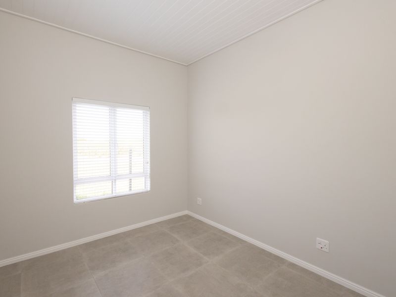A clean, empty bedroom featuring neutral wall tones, tiled flooring, and a tongue and groove ceiling, providing a versatile space ready for personalization.