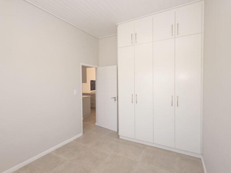 A clean, neutral bedroom featuring floor-to-ceiling built-in cupboards, modern tiled flooring, and a classic tongue and groove ceiling.