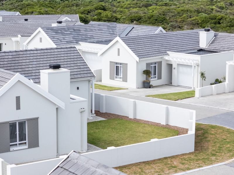 An aerial view of a modern residential estate featuring white-walled homes with grey tiled roofs, paved driveways, and manicured garden spaces.