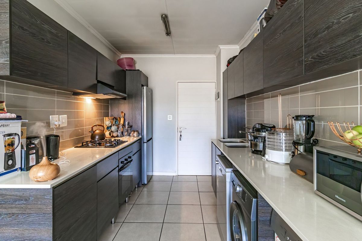 Modern galley-style kitchen featuring dark wood cabinetry, stone countertops, gas hob, extractor fan, and tiled finishes throughout.