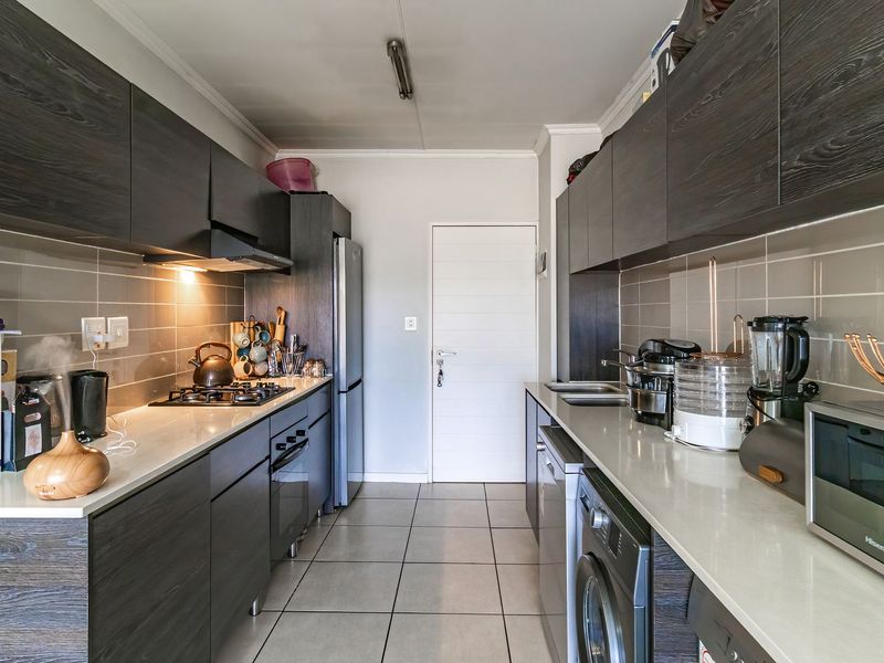 Modern galley-style kitchen featuring dark wood cabinetry, stone countertops, gas hob, extractor fan, and tiled finishes throughout.