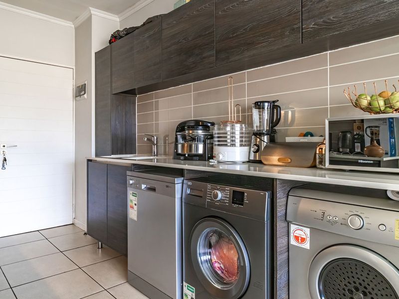 A modern, well-maintained laundry area featuring dark wood cabinetry, tiled backsplash, and integrated space for multiple appliances.