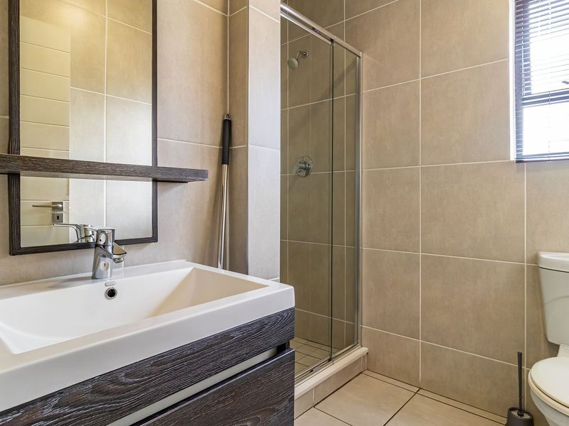 Modern bathroom featuring a vanity cabinet with basin, glass-enclosed shower, and neutral wall and floor tiling.