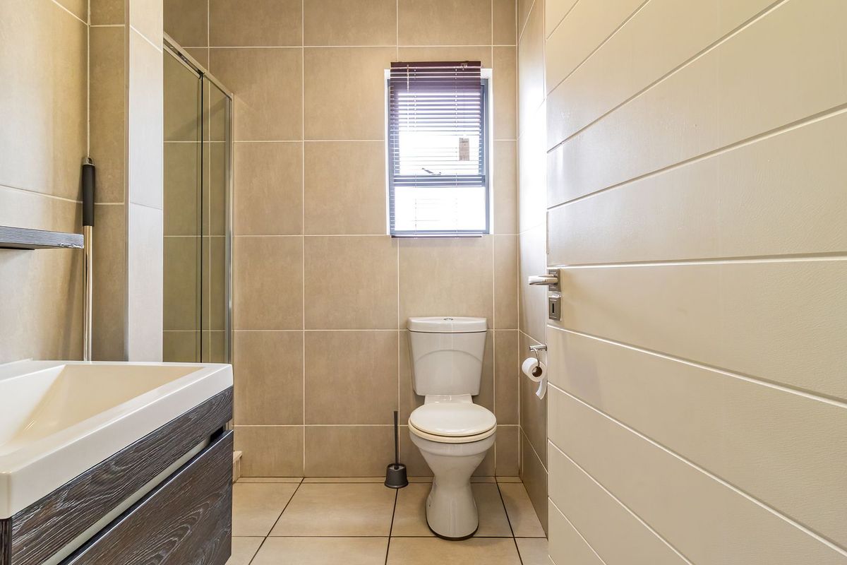 A modern, well-maintained bathroom featuring neutral wall and floor tiles, a vanity cabinet with a basin, a shower enclosure, and a toilet.