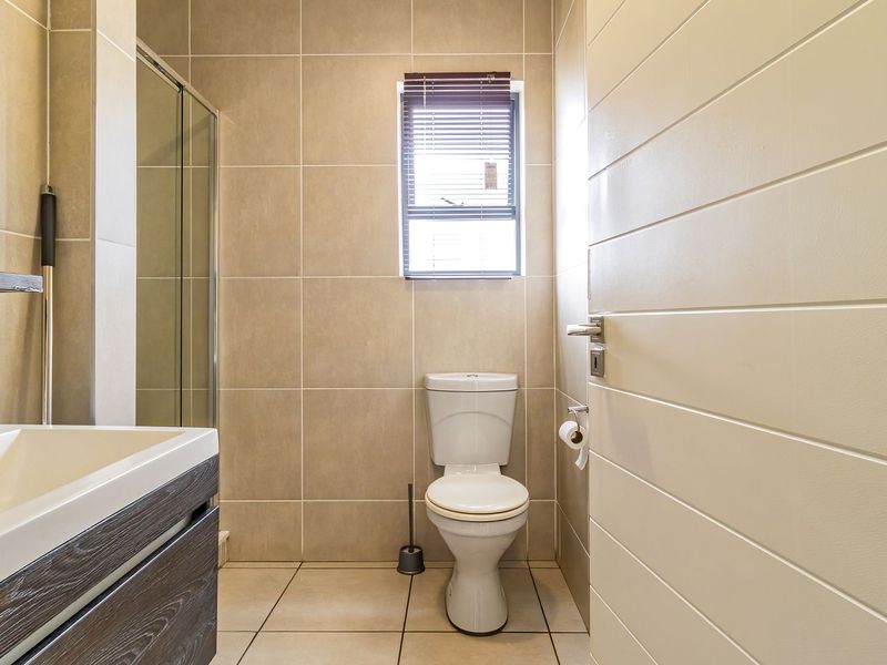 A modern, well-maintained bathroom featuring neutral wall and floor tiles, a vanity cabinet with a basin, a shower enclosure, and a toilet.