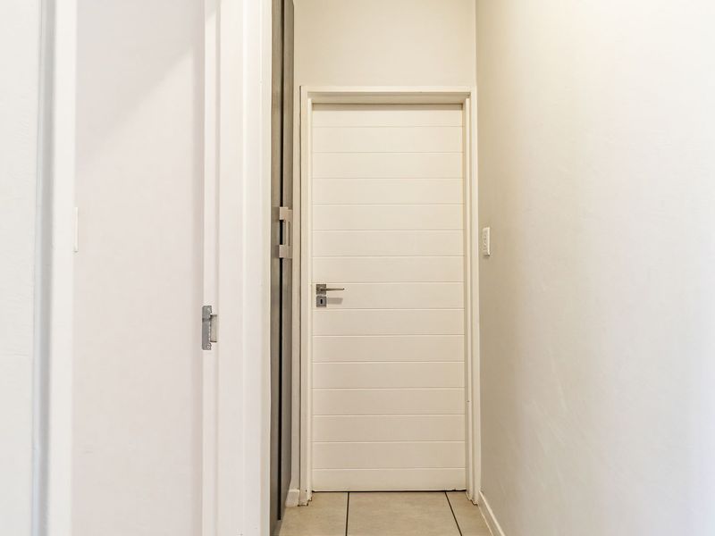 A clean and simple hallway featuring neutral wall finishes, tiled flooring, and a modern internal door.
