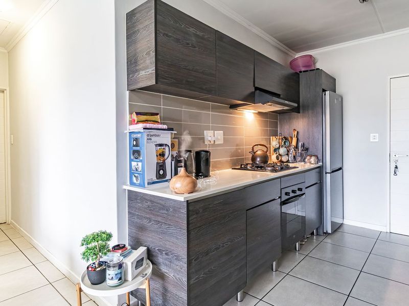 Modern kitchen featuring dark wood grain cabinetry, stone countertops, a gas hob with extractor fan, and neutral tiled flooring.