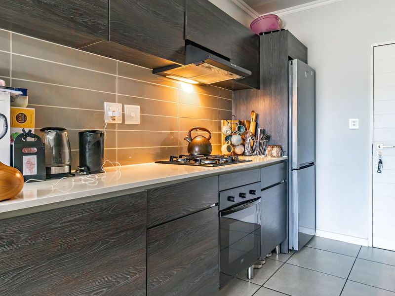 Modern kitchen featuring dark wood-grain cabinetry, stone countertops, a gas hob with extractor fan, and a tiled backsplash.