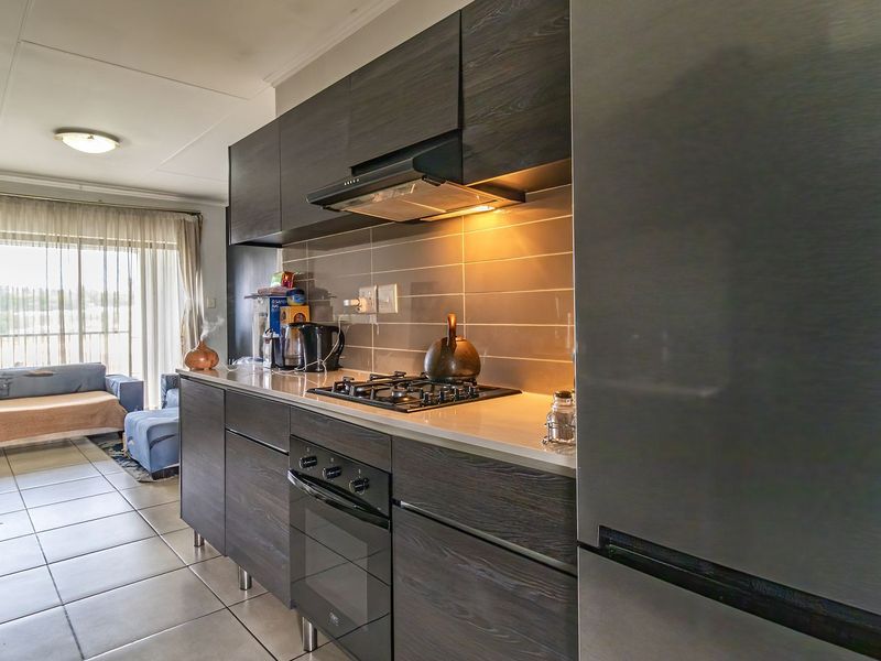 Modern open-plan kitchen featuring dark wood cabinetry, stone countertops, gas hob, and built-in oven, seamlessly flowing into the adjacent living area.