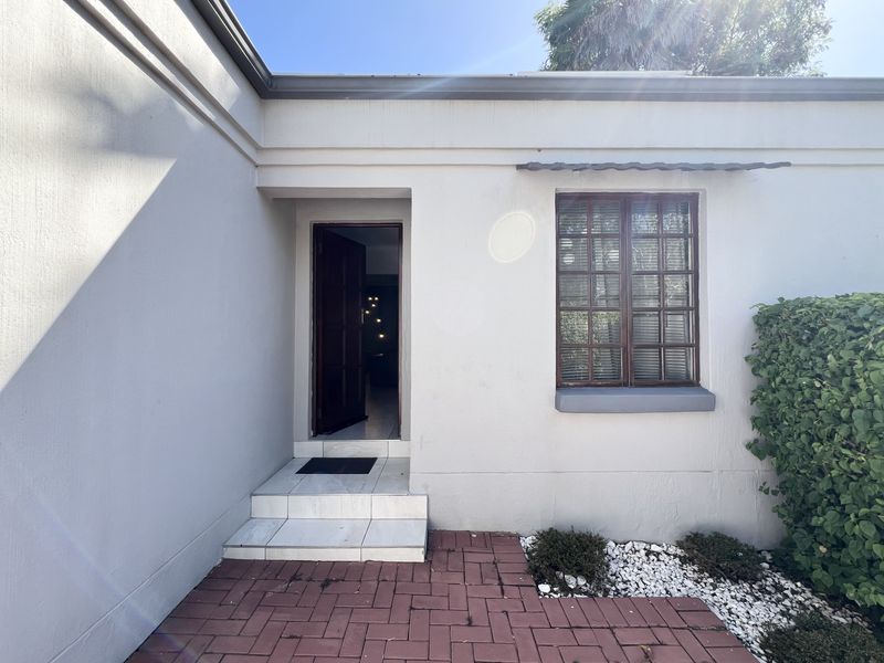 The front entrance of the townhouse features a paved patio area, tiled steps, and a timber-framed window, providing a welcoming and functional entry point.