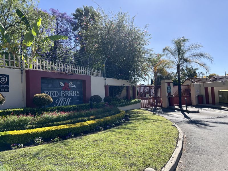 The entrance to Red Berry Hill complex featuring a secure gated access point, electric fencing, and well-maintained landscaped gardens.