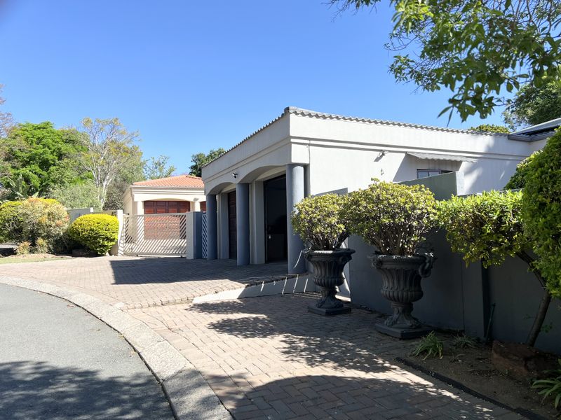 Front exterior view of the townhouse featuring a paved driveway, covered entrance with columns, and a secure boundary wall.