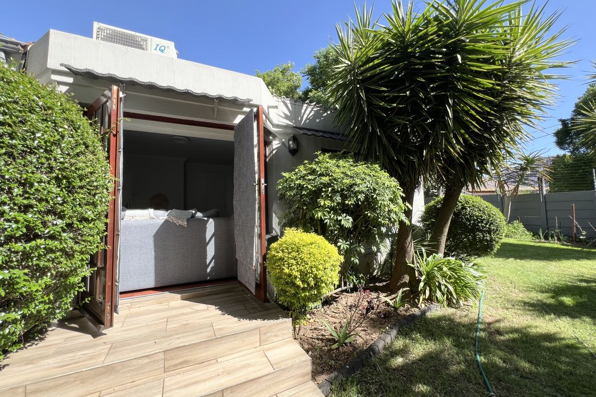 A well-maintained rear exterior featuring a tiled patio, double door access to the interior, and a landscaped garden area.