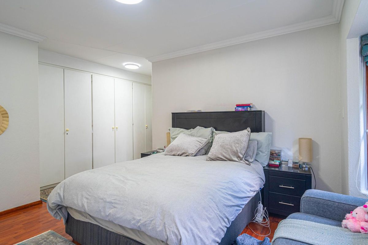 A bedroom featuring laminate flooring, built-in cupboards, and a window with natural light.