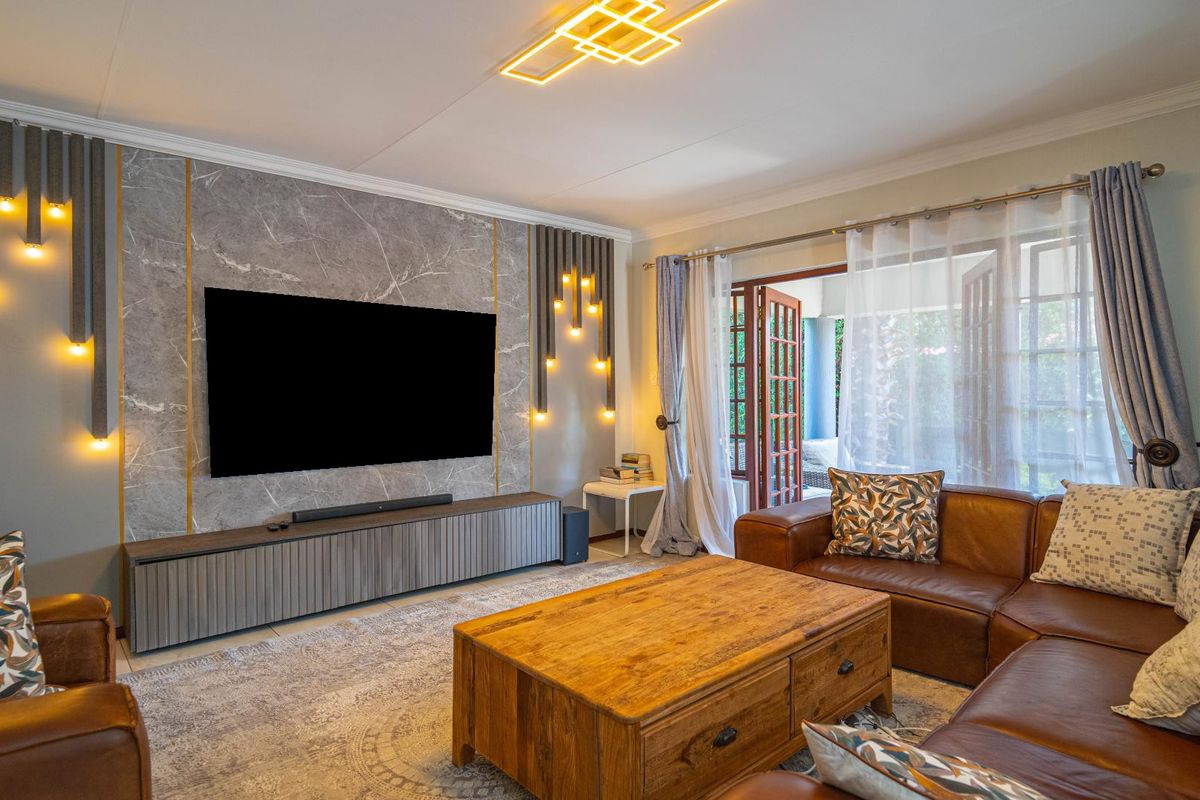 A well-appointed living room featuring a striking marble-look feature wall with integrated accent lighting, tiled floors, and direct access to the patio via french doors.