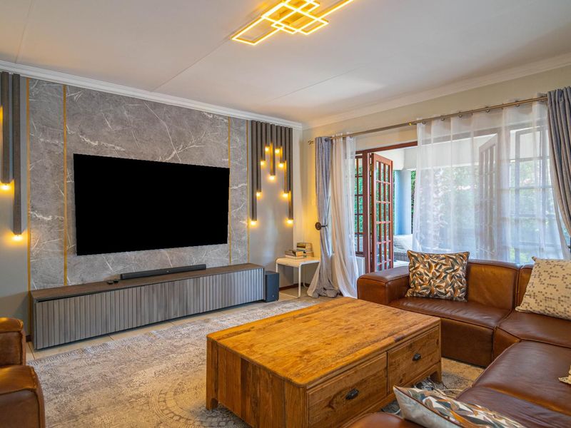 A well-appointed living room featuring a striking marble-look feature wall with integrated accent lighting, tiled floors, and direct access to the patio via french doors.