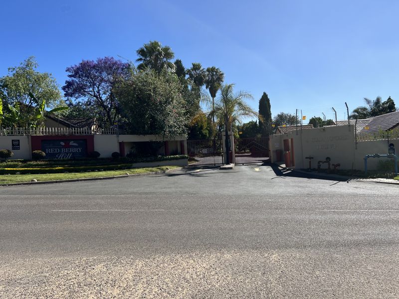Street view of the secure entrance to Red Berry Hill townhouse complex, featuring gated access, perimeter walling, and electric fencing.